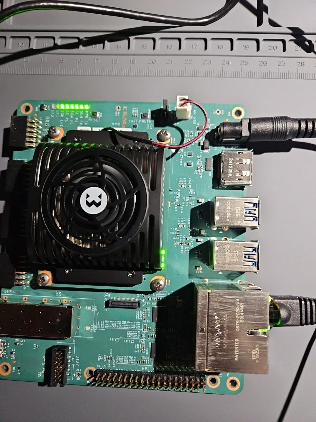 The AMD Kria KR260 board used for OCUP Phase I, powered on with status LEDs lit, on the AiCOMSCI workbench